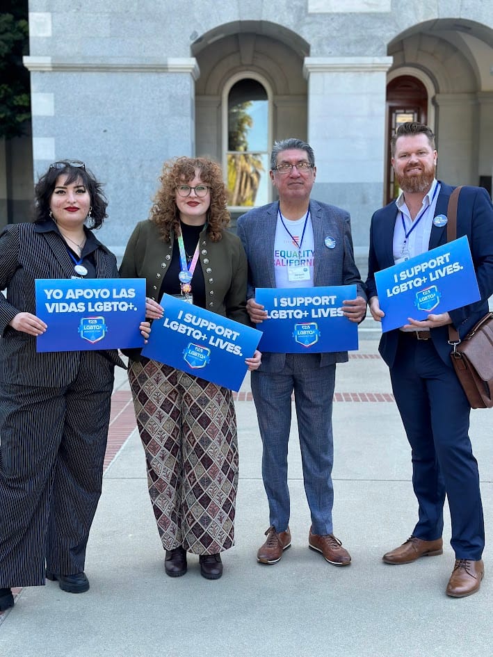 Four CalPride Directors stand holding signs advocating for LGBTQ+ rights. 